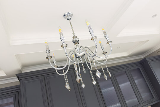 Modern chrome crystal chandelier illuminates white ceiling above dark cabinets