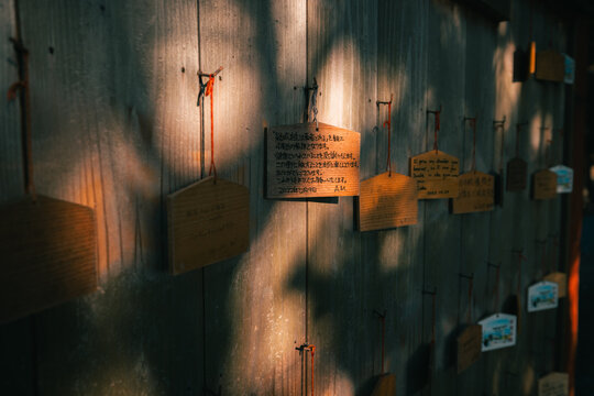 View of hanging wooden plaques with wishes cast shadows on a weathered wall, whispers of hope and dreams etched in a serene scene, Kanonji, Kagawa, Japan.