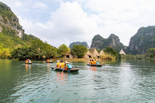 View of emerald waters reflecting the towering limestone karsts as boats carry tourists past the stilt houses in Trang An, Ninh Binh, Vietnam.