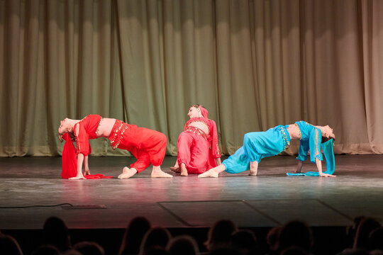 Three dancers performing odalisque-inspired backbend poses in colorful costumes on stage