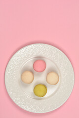 Obraz premium Four colorful macarons in pink beige and light green are arranged in a diamond shape on an ornate white ceramic plate against a pink background