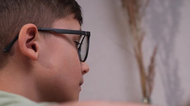 Young boy wearing black framed glasses, concentrating on a task or studying, capturing a moment of focused learning and intellectual development from a side profile