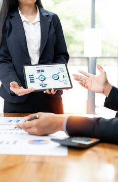 A collaborative business team presents a data-driven financial plan diagram on a tablet during a strategy session at a modern wooden desk with analysis reports and a calculator.