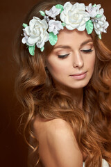 Fototapeta premium Close-up of a beautiful portrait of a young girl with a flower wreath in her hair. She is wearing a delicate flower crown with green leaves. The concept of beauty, spa, manicure, and skin care