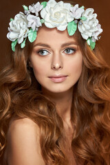 Naklejka premium Close-up of a beautiful portrait of a young girl with a flower wreath in her hair. She is wearing a delicate flower crown with green leaves. The concept of beauty, spa, manicure, and skin care
