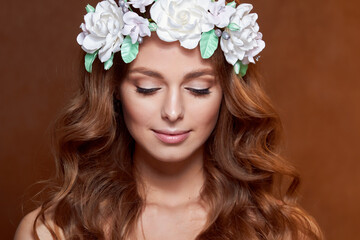 Naklejka premium Close-up of a beautiful portrait of a young girl with a flower wreath in her hair. She is wearing a delicate flower crown with green leaves. The concept of beauty, spa, manicure, and skin care