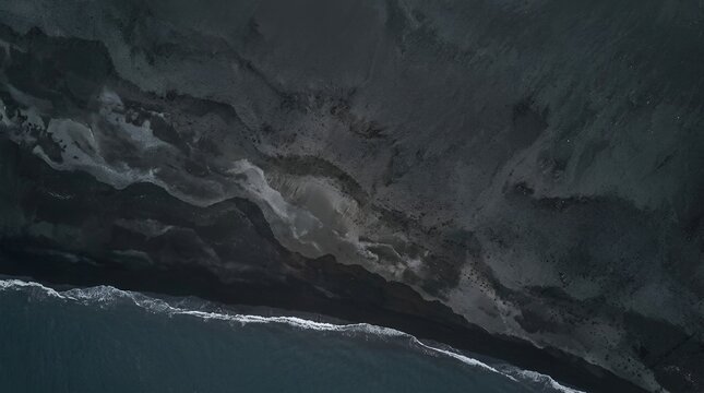 An awe-inspiring aerial perspective reveals the dramatic contrast of dark black volcanic sand meeting the foamy white crests of ocean waves, creating a mesmerizing natural pattern along the rugged coa