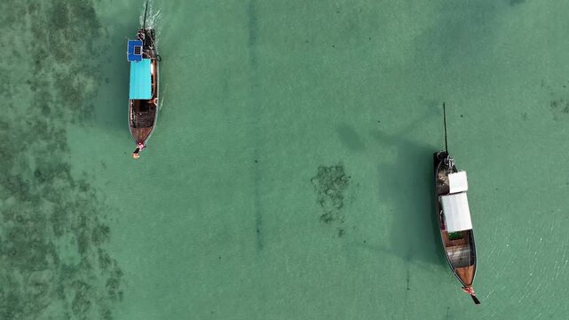 Aerial view of two longtail boats, one with a turquoise roof, sailing on the clear turquoise water, creating a stunning contrast of colors, Kho Phi Phi Island, Thailand.