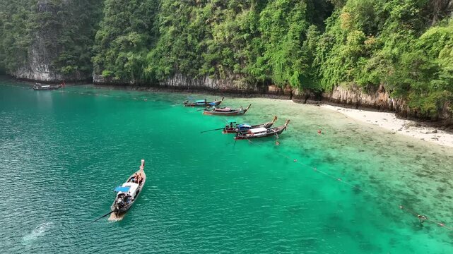 Aerial view of boats on clear turquoise waters meets lush green cliffs, creating a vibrant contrast of color and textures, Kho Phi Phi Island, Thailand.