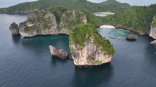 Aerial view of jagged islands covered in lush greenery standing in contrast to the dark blue sea, with a beach tucked away in a cove, Halong Bay, Vietnam.