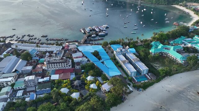 Aerial view of boats docked near buildings with distinctive blue roofs, contrasting with the lush greenery, Halong Bay, Vietnam.