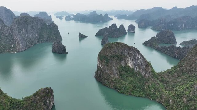 Aerial view of the stunning, jagged limestone karsts rising from the tranquil turquoise waters of Halong Bay, Vietnam, creating a dramatic seascape, Halong Bay, Vietnam.