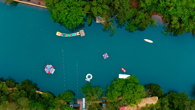 Aerial view of azure river reflecting the sky, lush greenery embracing its banks, and colorful floating platforms dotting its surface, Dark Cave, Qung Binh, Vietnam.