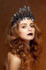 Fototapeta premium Close-up portrait of a beautiful young girl with a flower wreath in her hair. She wears a delicate flower crown with dark leaves. Beauty, spa, manicure and skin care concept