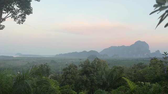 Morning scene over green forest and distant limestone hills at Din Daeng Doi in Krabi Thailand with soft sunlight, light haze, and peaceful tropical landscape atmosphere