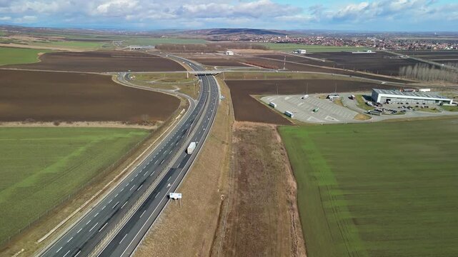 Sziksz&oacute;, Hungary&rsquo;s M30 motorway and highway junction traverse rural farmland and meadows near the urban edge, with vehicles, trucks, and service areas visible in this aerial bird&rsquo;s-eye view.
