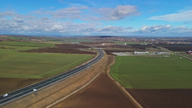 Sziksz&oacute;, Hungary&rsquo;s M30 motorway interchange and service area span rural farmland and village outskirts, with cars and trucks visible on asphalt roads in a panoramic aerial daytime view.