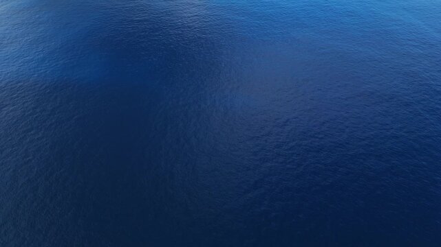 Top down aerial drone reveal of deep blue Caribbean ocean water surface and island coastline in distance