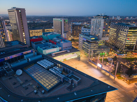Aerial perspective looking down onto the complex rooftops and modern architecture of MediaCityUK in Salford Quays, featuring the BBC buildings and the central plaza at dusk.