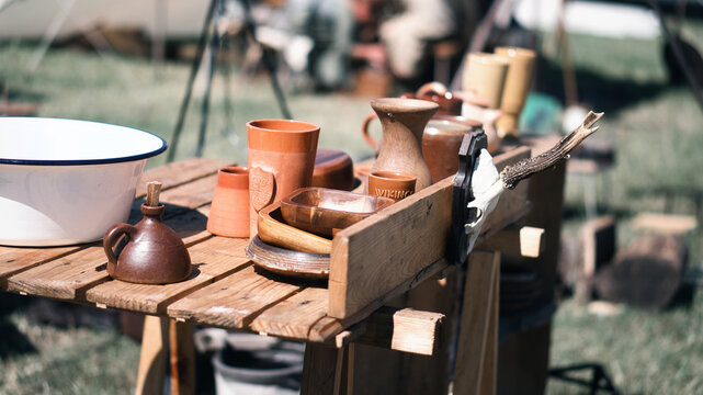 Close-up of historical crafts on a wooden table at a medieval market, featuring clay mugs, wooden bowls, and an enamel basin.