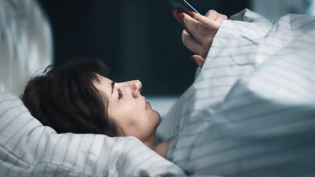 cinematic sleepy pretty woman lies on the bed and uses the phone, read some news, an evening alone, have fun and enjoy