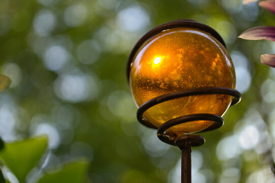 Decorative Amber Glass Garden Sphere Held By A Metal Spiral In The Sunlight