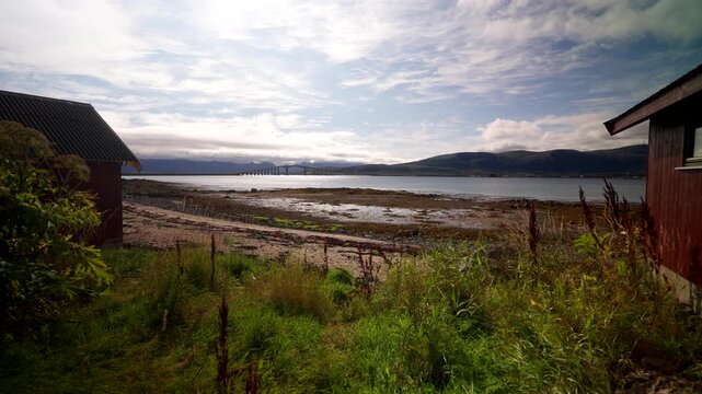 Coastal shoreline and Hadsel Bridge crossing fjord near Stokmarknes in northern Norway, wide establishing over overgrown home backyard