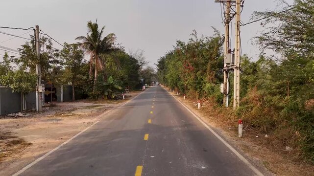 Aerial view of a road stretching into the distance, flanked by lush trees, with a motorbike in motion, under a bright sky, Tonle Sap Lake, Cambodia.