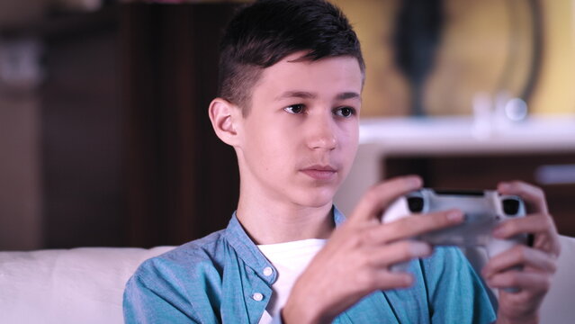 serious teen boy sitting on the sofa and plays a game on a console, have fun and enjoy