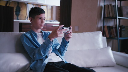 serious teen boy sitting on the sofa and plays a game on a console, have fun and enjoy © vla