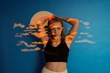 Obraz premium Woman posing with abstract sunset light projection on blue wall