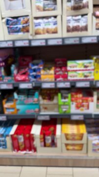 Blurred grocery aisle with colorful snack packages, blurred movement over tiled floor, packed shelves of chocolate, biscuits and candy in supermarket