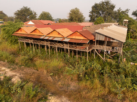 Aerial view of stilted houses perched above the verdant landscape, their red and brown roofs contrasting with the lush greenery below, Tonle Sap, Cambodia.