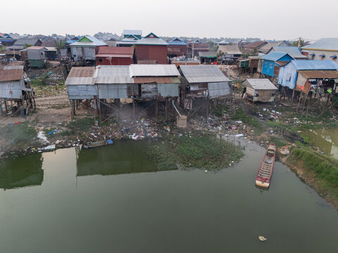 Aerial view of stilted houses crowded along the Tonle Sap's edge reflect in the water, a blend of rustic charm and the realities of waterside living, Tonle Sap, Cambodia.