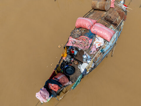 Aerial view of a boat laden with goods navigates the muddy waters, casting a reflection of daily life on the river, Tonle Sap, Cambodia.