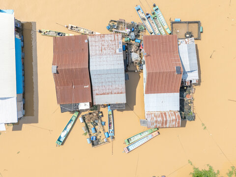 Aerial view of stilted buildings rise from the muddy waters, with boats clustered around homes, offering a glimpse into life adapted to the rhythms of the river, Tonle Sap, Cambodia.