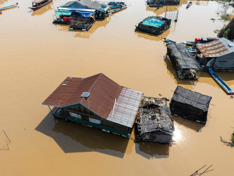 Aerial view of stilt houses rise from the muddy waters, reflecting the overcast sky, a testament to life adapted to the ebb and flow of the great lake, Tonle Sap, Cambodia.