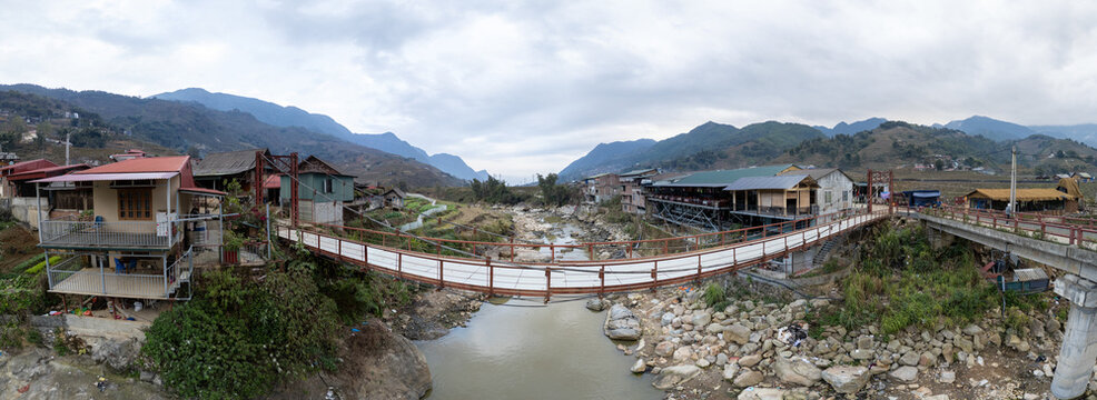 Aerial view of a quaint village nestled between verdant mountains, connected by rustic bridges over a flowing river, Sa Pa, Vietnam.