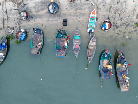 Aerial view of fishing boats resting on the sandy shore, their vibrant colors contrasting with the muted tones of the surrounding landscape, Da Nang, Vietnam.