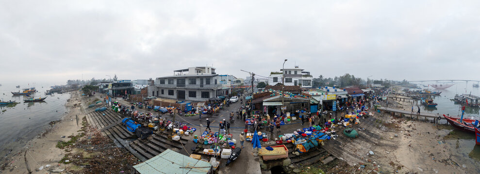 Aerial view of a bustling market by the water with colorful goods and boats lining the shore, Da Nang, Vietnam.