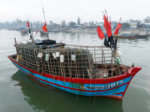 Aerial view of a fishing boat with red flags and nets, its blue and red hull reflecting on the calm water, Da Nang, Vietnam.