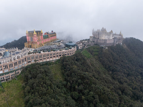Aerial view of a whimsical castle with vibrant hues piercing through the mist-shrouded peaks, like a fairy tale emerging from the clouds, Ba Na Hills, Vietnam.