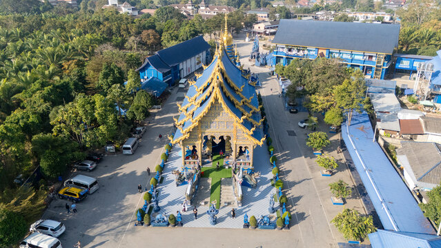 Aerial view of the striking blue temple, Wat Rong Suea Ten, rising amidst lush greenery and clear skies, its golden accents gleaming brightly, Chiang Rai, Thailand.
