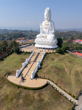 Aerial view of the immense white Buddha statue atop a verdant hill, the steps leading to it like a celestial staircase, Wat Phra That Doi Kham, Chiang Mai, Thailand.