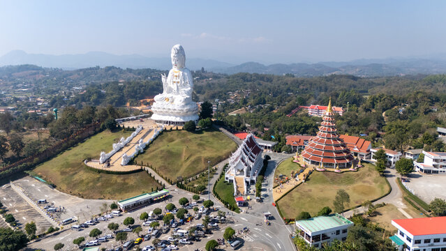 Aerial view of the majestic white Buddha statue atop the hill surrounded by lush greenery, Wat Phra That Doi Kham Buda Temple, Chiang Mai, Thailand.
