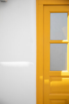View of a vibrant yellow door standing out against the stark white wall, creating a striking contrast in the sun-soaked streets, Mykonos, Greece.