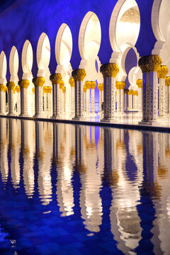 View of ornate white columns with golden accents reflected in the still, blue water, creating a mesmerizing symmetrical pattern, Abu Dhabi, United Arab Emirates.