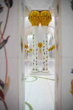 View of ornate white columns adorned with golden capitals and colorful floral inlays create a majestic corridor, a testament to architectural grandeur, Abu Dhabi, United Arab Emirates.