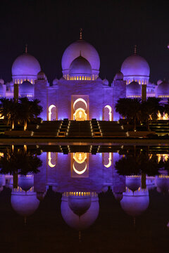View of the majestic Sheikh Zayed Mosque's illuminated domes and arches reflected in the tranquil water, a serene spectacle at night, Abu Dhabi, United Arab Emirates.