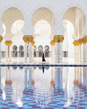 View of the Sheikh Zayed Mosque's pristine white arches mirrored in the reflecting pool, as a solitary figure walks by, Abu Dhabi, United Arab Emirates.